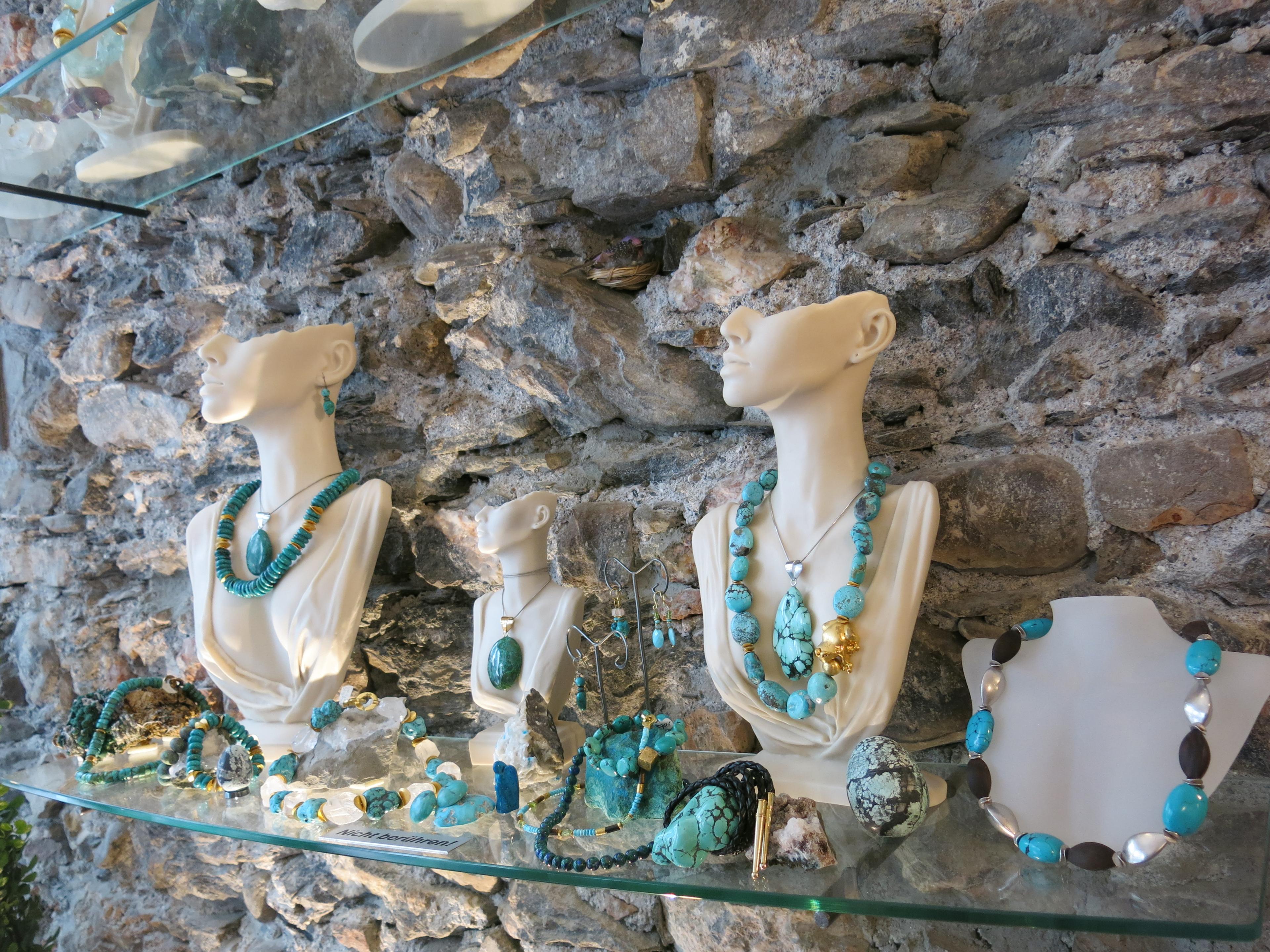 Türkisfarbene Edelstein-Ketten auf Büsten vor historischer Steinmauer